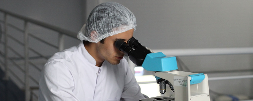 Mann schaut im Labor durch ein Mikroskop